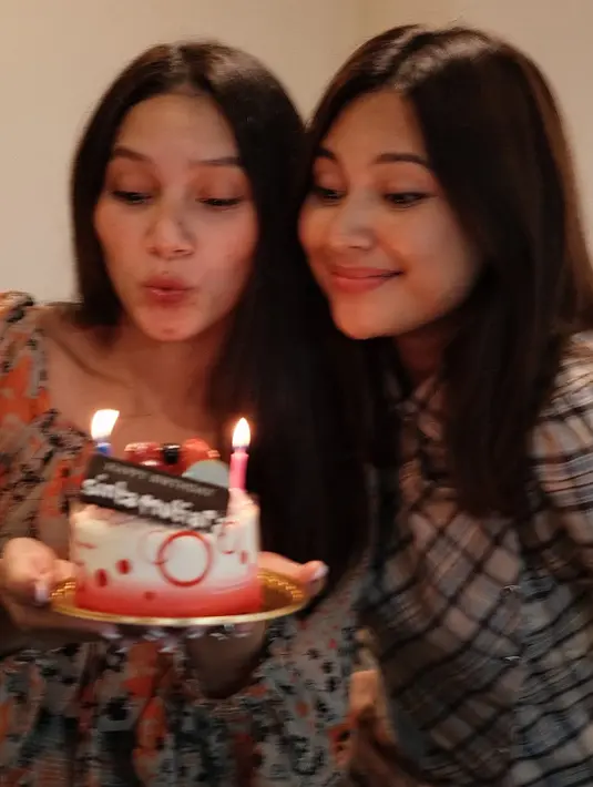 Indah tampak memberikan kue merah yang tidak terlalu besar lengkap dengan lilinnya. Terlihat kedua adik kakak ini memiliki rambut panjang terurai tanpa poni. [@indahpermatas]