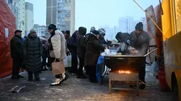 Terdampak pemadaman listrik dan air, warga Kyiv terlihat mengantre untuk mendapatkan makanan hangat di tengah kondisi musim dingin yang ekstrem. Tampak dalam foto, para sukarelawan dari organisasi amal makanan yang berbasis di Amerika Serikat (AS), World Central Kitchen, membagikan makanan hangat kepada warga setempat di sebuah kawasan perumahan di Kyiv yang mengalami pemadaman listrik dan air akibat serangan Rusia yang menghantam sektor energi, Kamis 22 Januari 2026. (Sergei GAPON/AFP)
