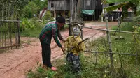 Seorang perempuan mendirikan orang-orangan sawah di depan rumahnya di provinsi Kampong Cham, Kamboja, 11 Oktober 2020. Penduduk di desa itu mebuat orang-orangan sawah atau disebut juga Tim Mong untuk menangkal virus corona  Covid-19 berdasarkan kepercayaan yang mereka yakini. (TANG CHHIN Sothy/AFP)