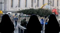 Biarawati mengamati pohon Natal raksasa yang hendak didirikan di Lapangan Santo Petrus, Vatikan, Kamis (22/11). Tahun ini, pohon Natal itu baru akan diresmikan pada 7 Desember dan lampunya tetap menyala hingga 13 Januari 2019. (AP/Andrew Medichini)