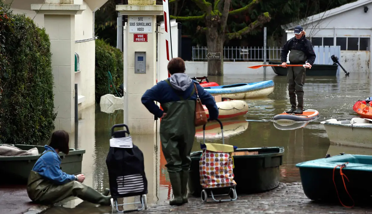 Seorang pria menggunakan papan dayung saat banjir melanda di jalan banjir di pulau Vaux, sebelah barat Paris, (30/1). Sungai Seine yang meluap akibat hujan deras dalam 50 tahun telah menelan dermaga di Paris, Prancis. (AP Photo / Thibault Camus)
