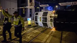 Petugas kepolisian memblokir lokasi sebuah trem double-decker yang terbalik di jalan utama di Hong Kong, Kamis (6/4). Hong Kong telah mengoperasikan tram, yang dikenal sebagai 'ding-ding' lebih dari satu abad lalu. (ANTHONY WALLACE/AFP)