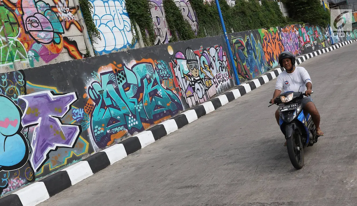 Pengendara melintasi jalur inspeksi Sungai Ciliwung di Jakarta, Kamis (27/12). Mural yang dibuat oleh beberapa komunitas tersebut menjadikan jalur inspeksi Sungai Ciliwung tampak lebih berwarna dan asri. (Liputan6.com/Immanuel Antonius)