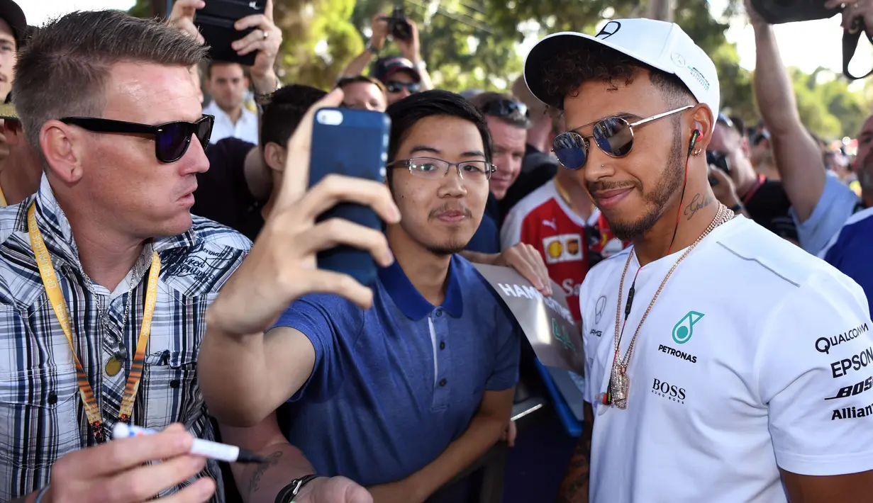 Pembalap Mercedes, Lewis Hamilton melakukan selfie dengan seorang penggemar menjelang sesi latihan bebas pertama di Grand Prix Australia, Melbourne, Jumat (24/3). (AFP Photo/WILLIAM WEST)