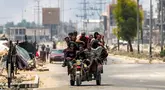 Para pria berkendara bersama di belakang gerobak roda tiga di sepanjang jalan Salaheddin, Deir el-Balah, Jalur Gaza tengah pada 21 Juli 2025, sementara di belakangnya mengepul asap akibat pemboman Israel. (Eyad BABA/AFP)