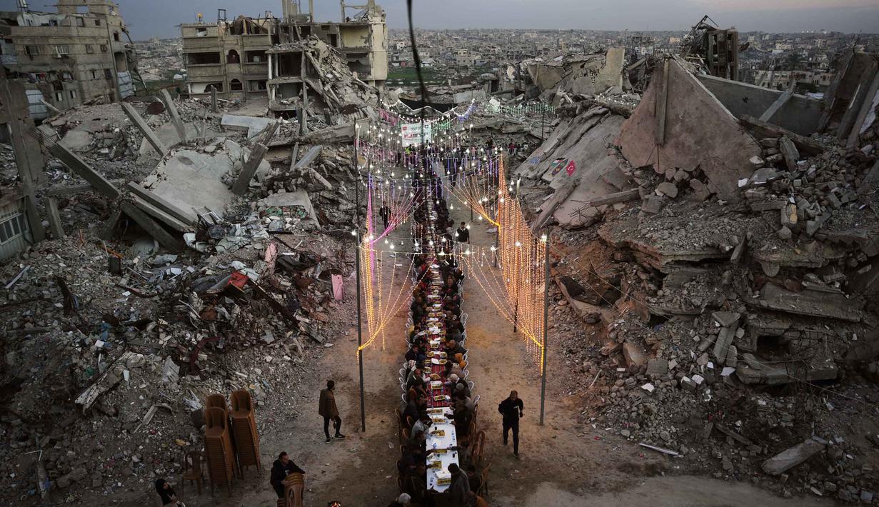 Dekorasi sederhana khas Ramadan tetap dipasang oleh warga Palestina di Gaza untuk menghadirkan suasana hangat dan solidaritas. Tampak dalam foto, warga Palestina duduk di meja panjang di tengah reruntuhan bangunan yang hancur untuk berbuka puasa bersama, selama bulan suci Ramadan di Khan Younis, Jalur Gaza, Kamis 19 Februari 2026. (AP Photo/Abdel Kareem Hana)