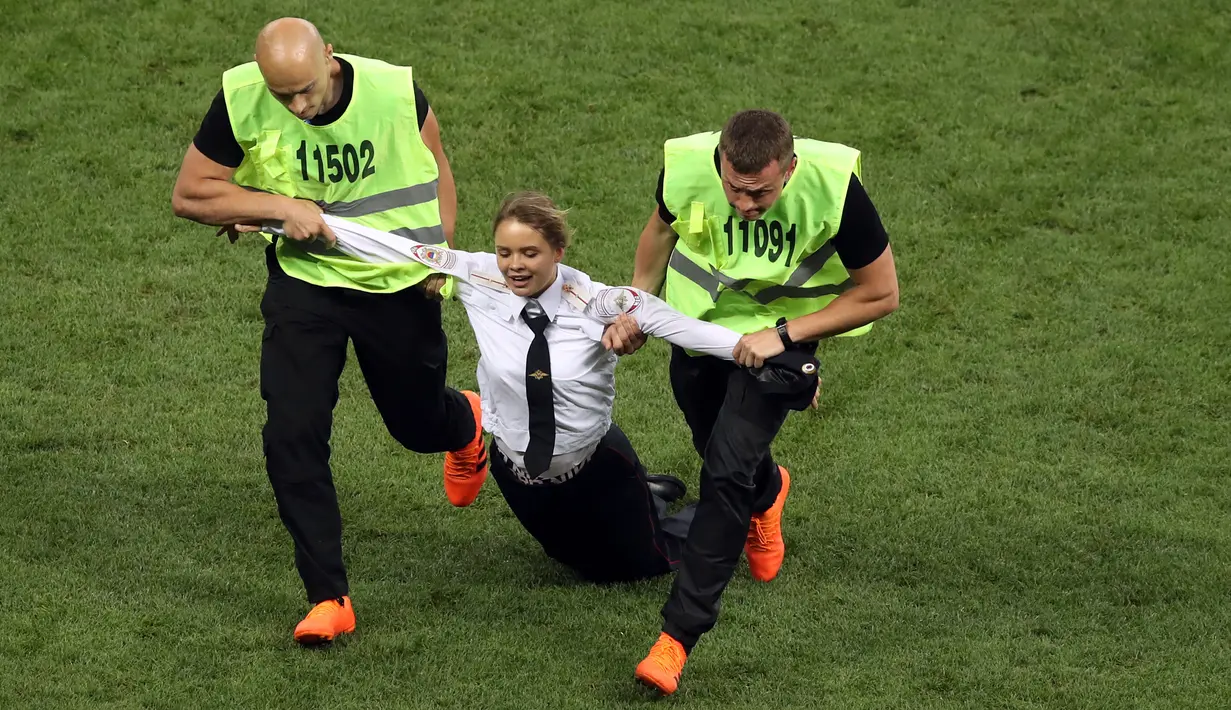 Petugas mengamankan seorang wanita yang menyusup masuk ke lapangan dalam laga final Piala Dunia 2018 antara Prancis dan Kroasia di Luzhniki Stadium, Minggu (15/7). Empat orang berlari masuk ke dalam lapangan menggangu jalannya laga. (AP/Martin Meissner)