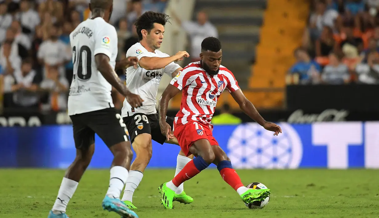 Penyerang Valencia, Fran Perez (tengah) berusaha merebut bola dari gelandang Atletico Madrid, Thomas Lemar (kanan) dalam pertandingan lanjutan La Liga Spanyol di stadion Mestalla di Valencia (30/8/2022). Atletico Madrid menang tipis atas tuan rumah Valencia 1-0. (AFP/Jose Jordan)