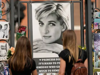 Dua wanita melihat potret Putri Diana dan kenangan lainnya yang dipajang di gerbang Istana Kensington, London, Selasa (30/8/2022). Minggu ini menandai peringatan 25 tahun kematian Putri Diana dalam kecelakaan mobil di Paris. (AP Photo/Alastair Grant)