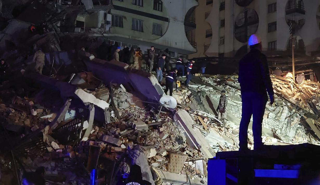 Orang-orang berusaha menjangkau warga yang terperangkap di sebuah bangunan yang runtuh di Diyarbakir, Turki tenggara, Senin dini hari, 6 Februari 2023. Kerusakan dilaporkan di beberapa provinsi Turki, dan tim penyelamat dikirim dari seluruh negeri. (AP Photo/Mahmut Bozarsan)