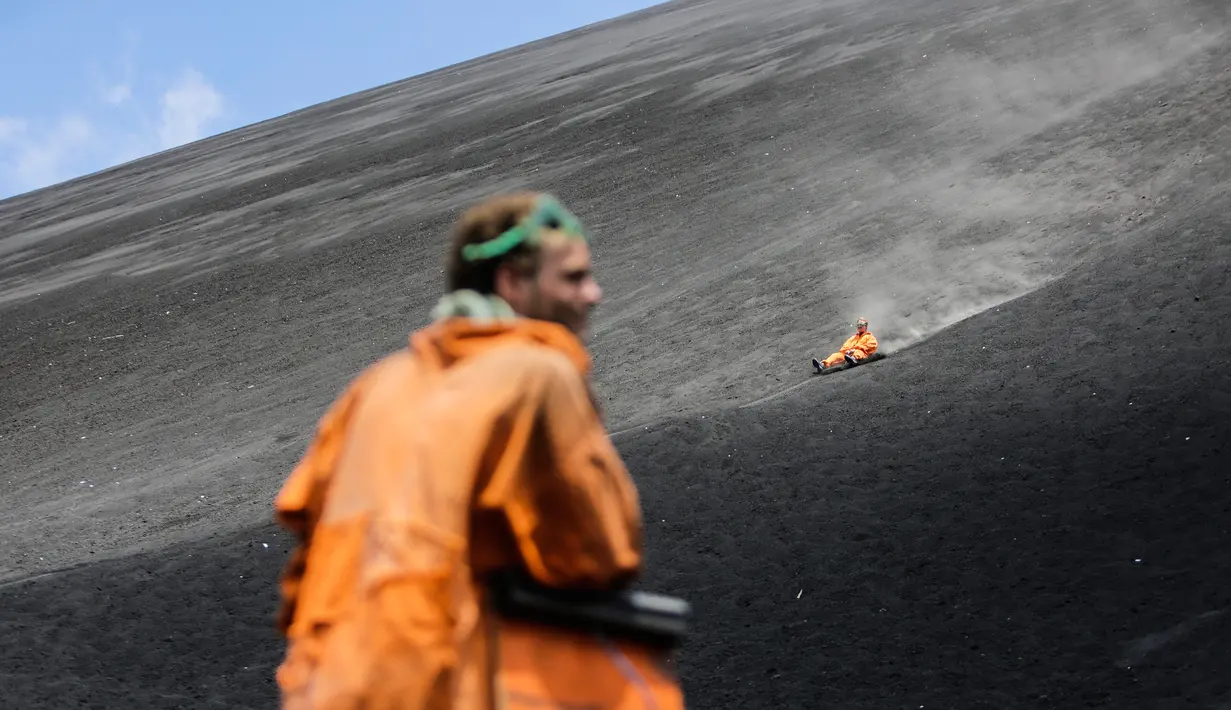 Seorang wisatawan memperhatikan rekannya yang bermain sandboarding atau berseluncur pasir menuruni gunung berapi Cerro Negro di Leon, Nikaragua, 24 September 2016. Gunung Cerro Negro salah satu gunung api yang masih aktif di Nikaragua. (INTI Ocon/AFP)