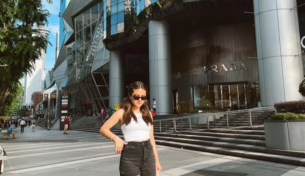 Liburan di Singapura, Marsha tampil dengan atasan tank top crop putih dipadukan celana pendek high waist hitam serta sneakers. [@aruanmarsha]