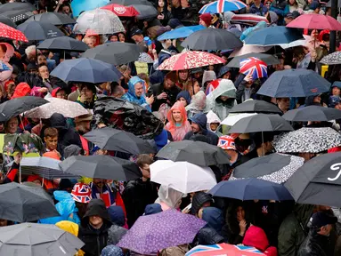 Para simpatisan berteduh dari hujan di bawah payung yang berjejer di sepanjang rute 'Prosesi Raja', yang membentang sejauh dua kilometer dari Istana Buckingham ke Westminster Abbey, sambil menunggu Raja Charles III dan Permaisuri Camilla, melintasi Diamond State Coach, di pusat kota London, Sabtu (6/5/2023). (Photo by PIROSCHKA VAN DE WOUW / POOL / AFP)