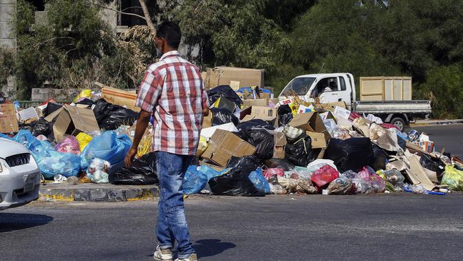 Seorang pria berjalan di dekat tumpukan sampah di sepanjang sisi jalan di Tripoli, ibukota Libya (30/9/2019). Muak dengan bau dan pemandangan tikus dan kucing liar, penduduk mengambil untuk membakar sampah, hanya untuk mengganti bau busuk dengan kolom asap yang memuakkan. (AFP Photo/Mahmud Turkia)