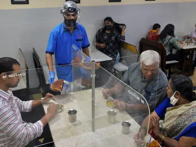 Pramusaji mengenakan pelindung wajah dan masker saat menyajikan makanan kepada pelanggan di restoran yang dibuka kembali usai pelonggaran lockdown di Bangalore, India, Senin (8/6/2020). Untuk keamanan pelanggan, restoran-restoran menyiapkan panel transparan di meja makan. (Manjunath Kiran/AFP)
