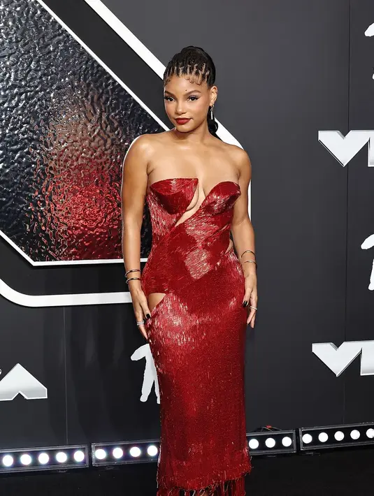 Halle Bailey tampil bersinar dalam gaun berwarna mawar detail potongan V-neck asimetris. Potongan lain diposisikan di sekitar pinggul kanannya sementara poni lucu menjuntai dari garis tepi sepanjang pergelangan kaki. Gaun tersebut menampilkan pengerjaan detail dengan deretan manik-manik berkilau yang disejajarkan dengan mulus untuk menciptakan estetika yang ramping dan glamor. [@mtv].