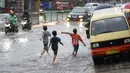 Anak-anak melintasi banjir yang menggenangi Jalan Arif Rahman Hakim di Depok, Jawa Barat, Senin (18/5/2020). Sistem drainase buruk menjadi penyebab utama kawasan tersebut selalu tergenang banjir setiap hujan deras. (Liputan6.com/Immanuel Antonius)