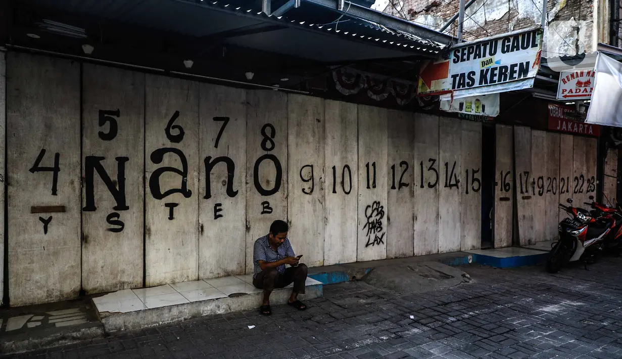Seorang pria duduk di di depan pertokoan kawasan perdagangan Pasar Baru yang tutup, Jakarta, Jumat (3/4/2020). Sebagian pemilik toko di Pasar Baru memilih menutup usahanya sementara waktu untuk mengantisipasi meluasnya penyebaran virus corona COVID-19. (Liputan6.com/Faizal Fanani)