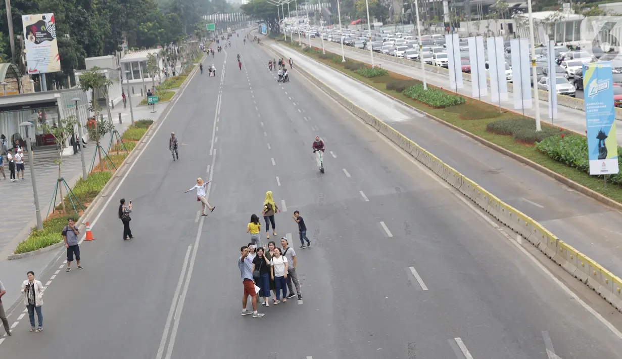 Warga memanfaatkan kondisi lengang sebagian ruas jalan Jenderal Sudirman untuk berfoto, Jakarta, Minggu (27/10/2019). Sebagian ruas Jalan Jenderal Sudirman dialihkan akibat  berlangsungnya Karnaval Kendaraan Listrik yang bertajuk Jakarta Langit Biru. (Liputan6.com/Helmi Fithriansyah)