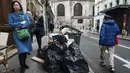 Orang-orang berjalan melewati sampah yang tidak diambil di Paris, Prancis, Senin (13/3/2023). Demonstrasi besar-besaran serta pemogokan bergilir di Paris dan kota-kota lain untuk menolak peraturan pensiun itu telah berdampak pada kilang, transportasi umum dan pengumpulan sampah. (AP Photo/Lewis Joly)