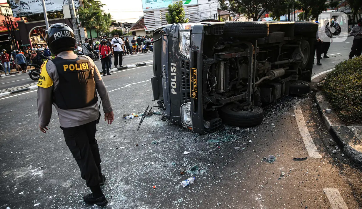 Polisi berjalan dekat sebuah mobil polisi yang dirusak massa saat bentrok di kawasan Pejompongan, Jakarta, Rabu (7/10/2020). (Liputan6.com/Faizal Fanani)