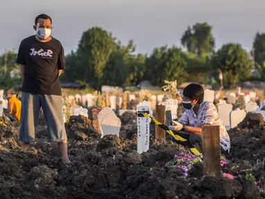 Keluarga berdoa untuk kerabat mereka di lokasi pemakaman korban virus corona COVID-19 di TPU Keputih, Surabaya, Jawa Timur, Sabtu (17/7/2021). Di Kota Surabaya terdapat dua tempat lahan pemakaman khusus blok COVID-19 yakni TPU Keputih dan TPU Babat Jerawat. (JUNI KRISWANTO/AFP)