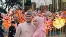 Kesha Ratuliu mengenakan kebaya brokat pink dipadukan kerudung pink polos dengan aksesori anting sebagai ciri khasnya. Sang suami juga mengenakan beskap coklat dipadukan kain batik. [@kesharatuliu05]