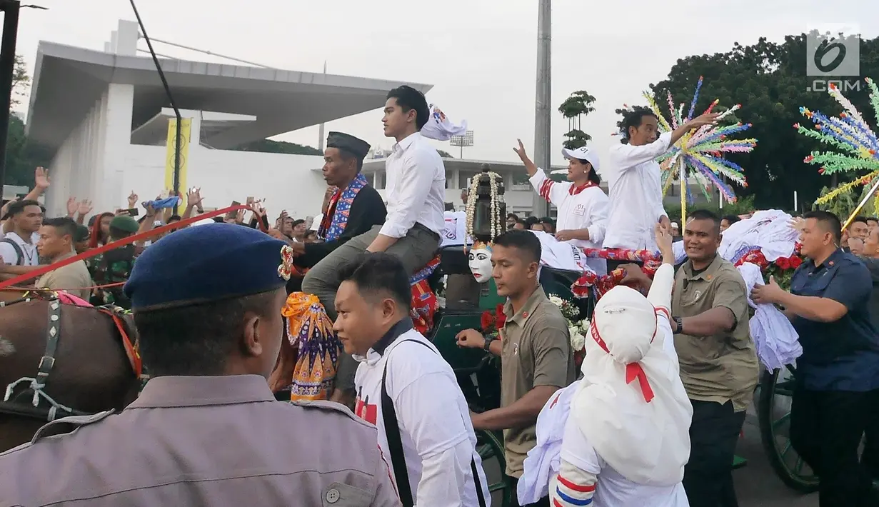 Capres 01 Joko Widodo didampingi Iriana Jokowi dan Kaesang Pangarep melempar kaus seusai 'Konser Putih Bersatu' di Stadion GBK, Jakarta, Sabtu (13/4). Pasangan Capres dan Cawapres 01 menggunakan kereta kencana seusai Konser Putih Bersatu menuju lokasi debat. (Liputan6.com/Herman Zakharia)