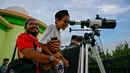 Untuk diketahui, metode rukyat sangat berbeda dengan hisab. Hisab murni menggunakan perhitungan matematis-astronomis tanpa memerlukan verifikasi visual di lapangan. Tampak dalam foto, seorang pria menggendong anaknya untuk mengamati bulan, menjelang Idul Fitri sekaligus menandai berakhirnya bulan suci Ramadan1447 Hijriah melalui teleskop di kantor observatorium, pantai Lhoknga, Aceh pada Kamis 19 Maret 2026. (CHAIDEER MAHYUDDIN/AFP)