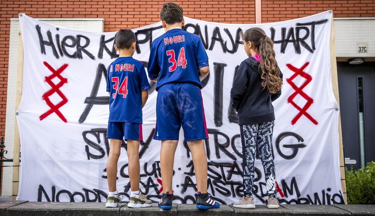 Fans menggunakan jesrsey nomor 34 milik Abdelhak Nouri berdiri di depan spanduk dukungan di Amsterdam, Kamis (13/7/2017). Pemain berusia 20 tahun ini terancam harus mengakhiri kariernya karena mengalami kerusakan otak permanen. (AFP/Bart Maat)