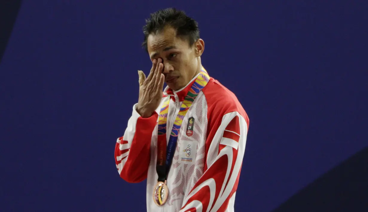 Lifter Suratman menangis saat naik podium usai mendapatkan medali perunggu SEA Games 2019 cabang angkat besi nomor 55 kg di Stadion Rizal Memorial, Manila, Minggu (1/12). Dirinya meraih perak dengan total angkatan 250 kg. (Bola.com/M Iqbal Ichsan)