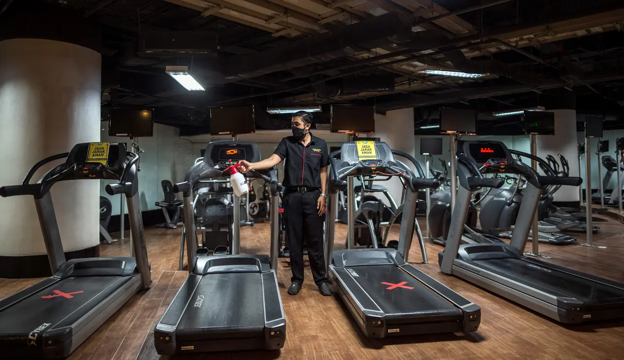 Seorang pria menyemprotkan disinfektan di sebuah tempat gym yang menerapkan jarak fisik di Surabaya, Rabu (21/10/2020). Pusat kebugaran itu dibuka dengan menerapkan protokol kesehatan sebagai pencegahan COVID-19. (Juni Kriswanto / AFP)