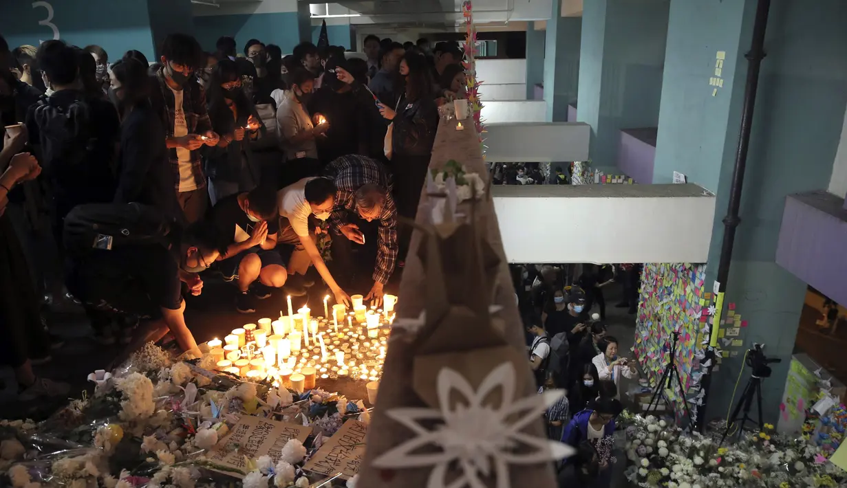 Para pengunjuk rasa menyalakan lilin dan meletakkan bunga di lokasi di mana mahasiswa Alex Chow Tsz-lok jatuh di Hong Kong (8/11/2019). Chow ditemukan terbaring dengan genangan darah di sebuah tempat parkir mobil, yang menjadi sasaran penembakan gas air mata oleh polisi. (AP Photo/Kin Cheung)