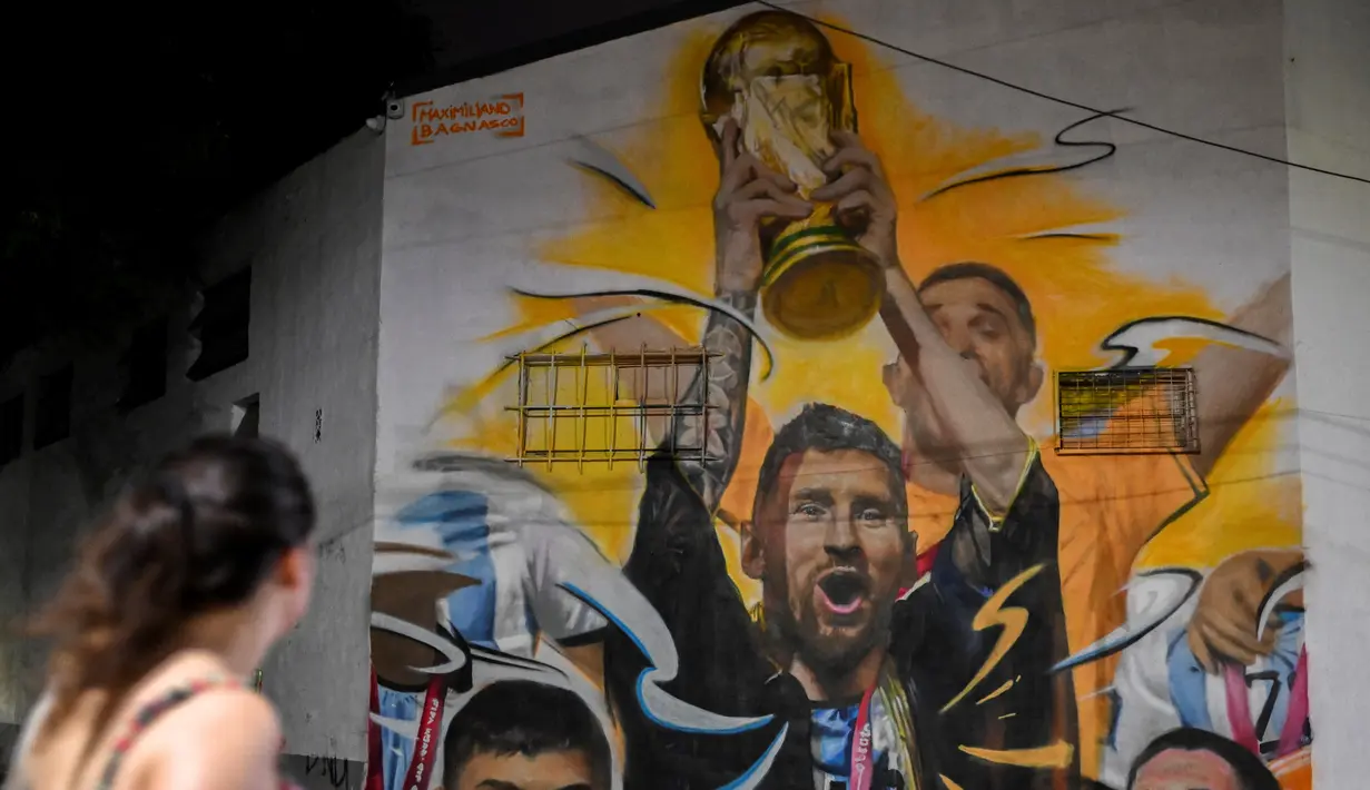 <p>Warga melihat Mural yang menggambarkan kapten dan penyerang Argentina Lionel Messi mengangkat Trofi Piala Dunia 2022 di samping rekan satu timnya setelah memenangkan turnamen Piala Dunia Qatar 2022 di Buenos Aires pada 22 Desember 2022. Argentina berhasil meraih juara setelah mengalahkan Prancis di babak final. (AFP/Luis Robayo)</p>