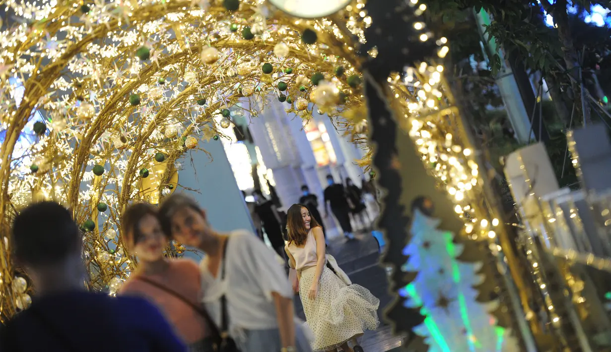 Orang-orang berpose untuk difoto dengan dekorasi lampu Natal di tengah hujan rintik di sepanjang pusat perbelanjaan Orchard Road di Singapura (16/12/2020). Sepanjang jalan di Orchard Road, dihiasi lampu hias, dedaunan artifisial khas natal dan dekorasi lainnya. (Xinhua/Then Chih Wey)