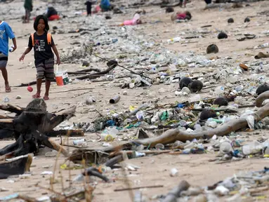 Anak-anak berjalan melewati plastik dan sampah lainnya yang terdampar di Pantai Kedonganan, Kabupaten Badung, Bali, Indonesia, Rabu (12/4/2023). (SONNY TUMBELAKA/AFP)