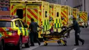 Paramedis mendorong troli dekat barisan ambulans di luar Rumah Sakit Royal London, Inggris, 6 Januari 2022. Inggris memangkas waktu isolasi pasien COVID-19 dari 10 menjadi 7 hari karena kekurangan tenaga kesehatan akibat lonjakan kasus yang dipicu Omicron. (AP Photo/Matt Dunham)