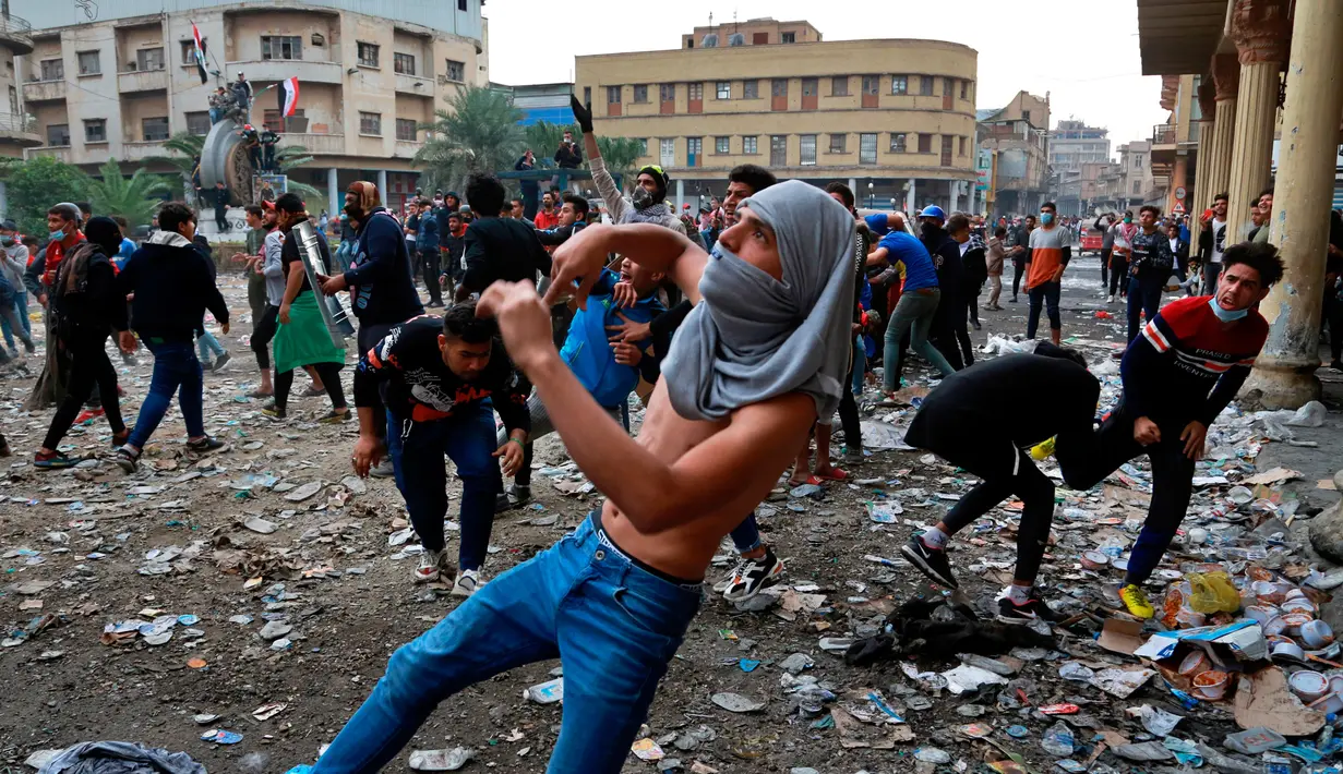 Demonstran antipemerintah melemparkan batu arah pasukan keamanan saat bentrok di Rasheed Street, Baghdad, Irak, Kamis (28/11/2019). Sebanyak 27 demonstran antipemerintah tewas ditembak mati oleh pasukan keamanan Irak dalam sehari. (AP Photo/Khalid Mohammed)