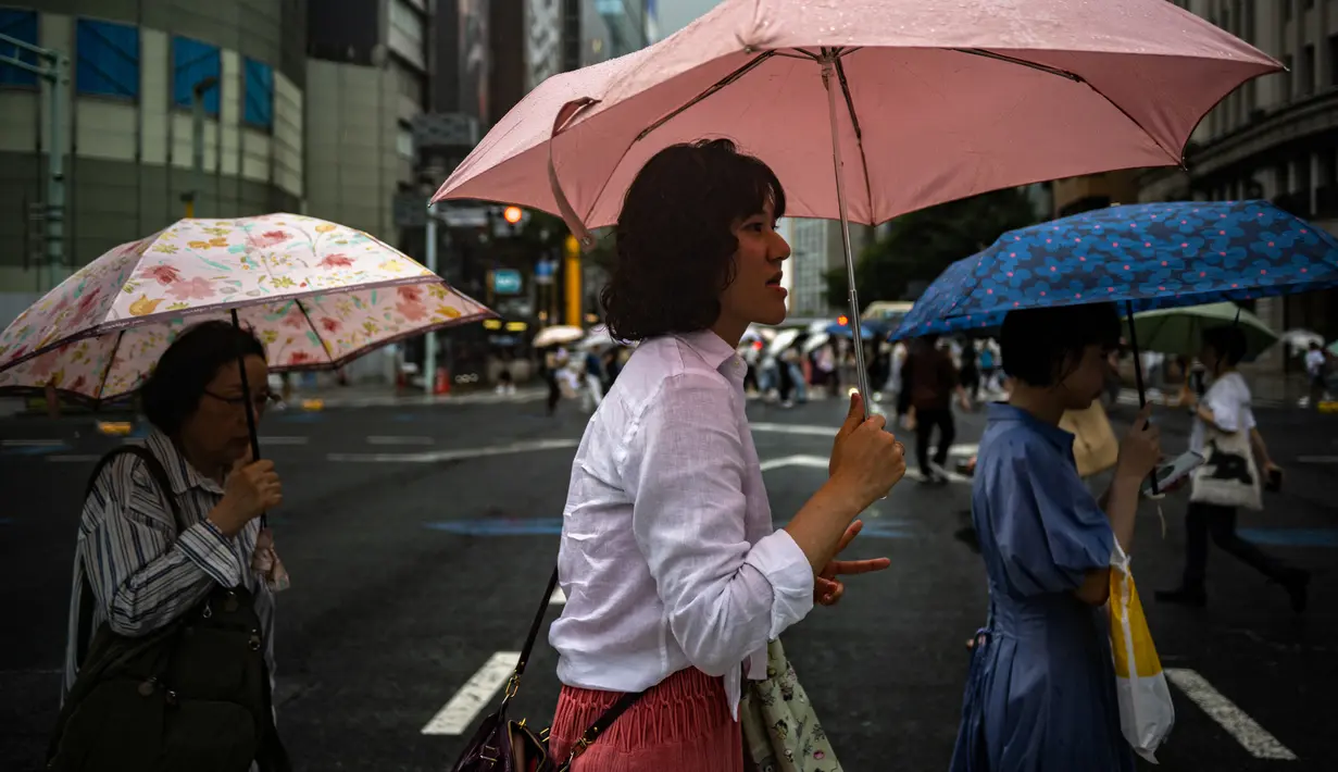 Pejalan kaki berjalan dengan payung di tengah hujan saat Topan Lan menuju pulau utama Jepang Honshu di distrik Ginza Tokyo pada 13 Agustus 2023. (AP Photo/Philip Fong)