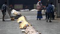 Warga berdiri dekat jasad korban virus corona COVID-19 yang akan dikremasi di tempat kremasi di New Delhi, India, Rabu (28/4/2021). Korban tewas akibat COVID-19 yang terus berjatuhan membuat jasad korban harus antre untuk dikremasi. (Money SHARMA/AFP)