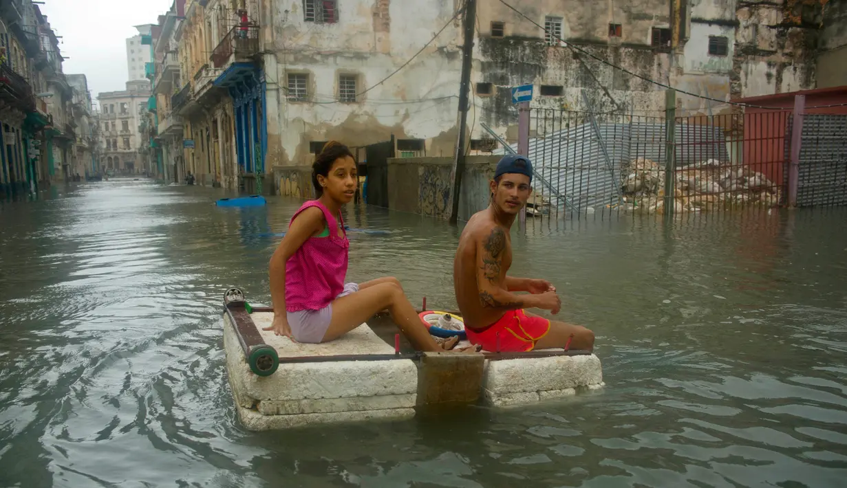 Sepasang warga menggunakan styrofoam untuk melewati jalanan yang terendam banjir di Hanava, Kuba, Minggu (10/9). Badai irma yang melanda pantai timur Perairan Kuba pada Jumat waktu setempat menyebabkan sebagian kota terendam banjir. (AP/Ramon Espinosa)