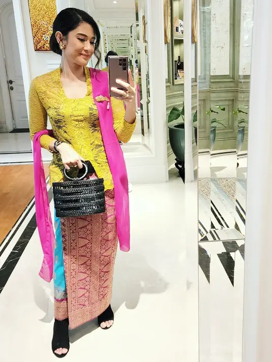 Kali ini, berfoto selfie di depan kaca, Dian Sastro menampakkan dirinya dalam balutan kebaya brokat berwarna hijau kekuningan, dipadu dengan selendang magenta, kain tenun sebagai bawahan, dan ia menenteng hand bag hitam. Aksesori berupa bros emas yang disematkannya di dadanya juga mempercantik penampilannya secara keseluruhan. Foto: Instagram.