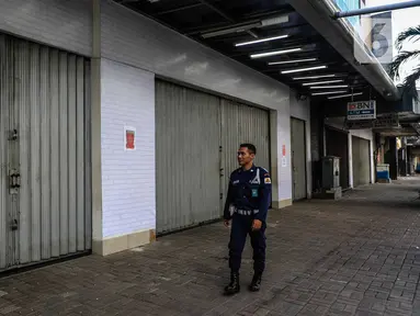 Petugas keamanan berjalan di depan pertokoan kawasan perdagangan Pasar Baru yang tutup, Jakarta, Jumat (3/4/2020). Sebagian pemilik toko di Pasar Baru memilih menutup usahanya sementara waktu untuk mengantisipasi meluasnya penyebaran virus corona COVID-19. (Liputan6.com/Faizal Fanani)