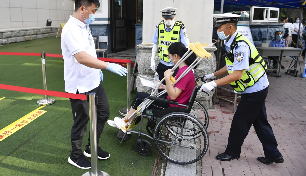 Seorang staf membantu peserta penyandang disabilitas memasuki lokasi ujian masuk perguruan tinggi di sekolah menengah atas di Changchun, ibu kota Provinsi Jilin, China timur laut (7/7/2020). Ujian masuk perguruan tinggi nasional China tahun ini telah dimulai pada Selasa (7/7). (Xinhua/Xu Chang)