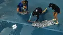 Para ball boy mengeringkan lapangan saat hujan menunda pertandingan perempat final kejuaraan tenis Australia Open 2023 di Melbourne, Selasa (24/1/2023). Gelaran turnamen grand slam Australia Open 2023 kembali dihentikan untuk beberapa saat setelah hujan mengguyur Melbourne Park. (AP Photo/Ng Han Guan)