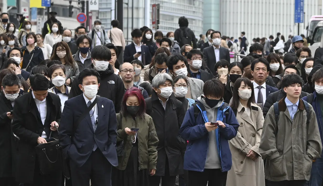 Komuter menunggu lampu lalu lintas di persimpangan di distrik Shinjuku Tokyo pada hari pertama pemerintah Jepang mencabut ketentuan wajib mengenakan masker, Senin (13/3/2023). Meski begitu, pemerintah Jepang masih merekomendasikan penggunaan masker di dalam ruangan dan tidak diwajibkan untuk di luar ruangan. (Photo by Kazuhiro NOGI / AFP)