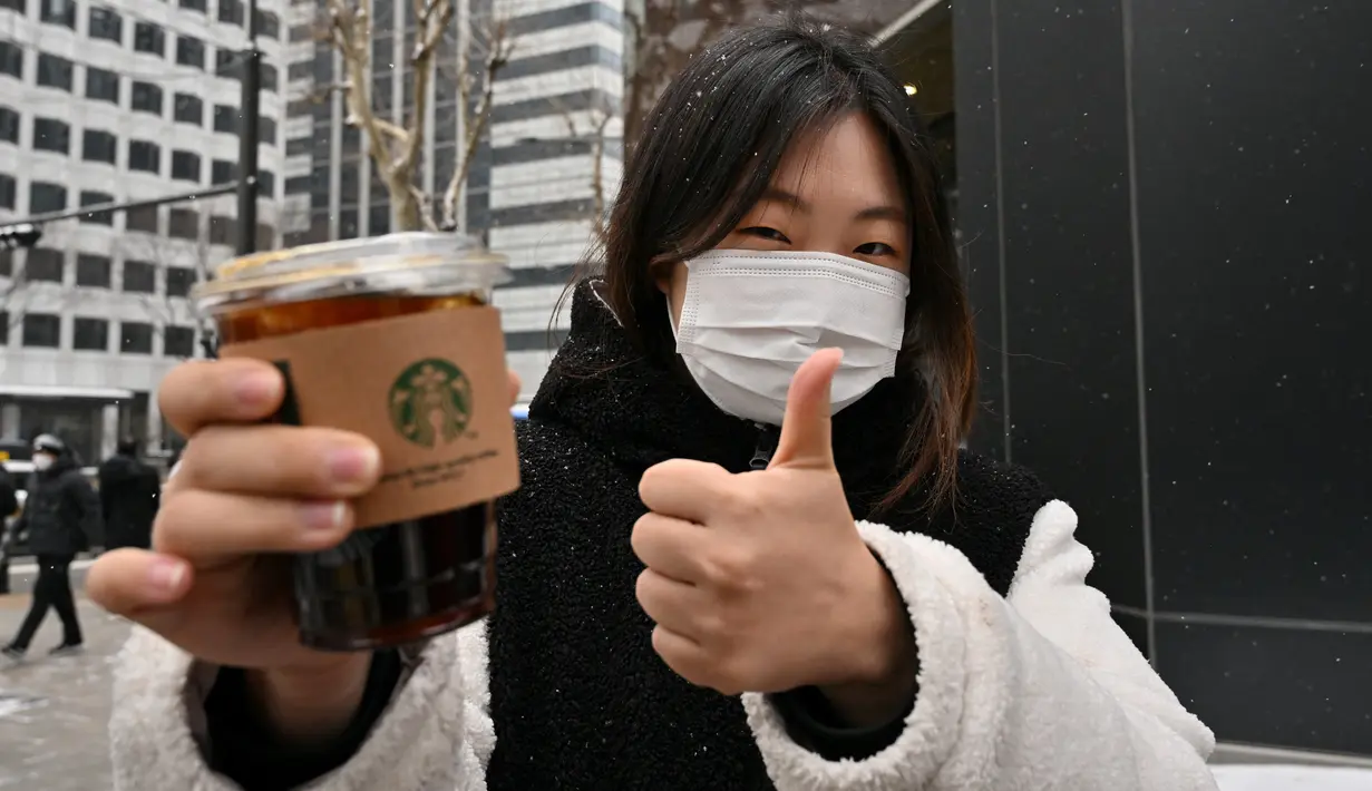 Foto yang diambil pada 26 Januari 2023 ini menunjukkan pekerja kantoran Jeong Jae-won berpose dengan es Americano selama wawancara dengan AFP di sebuah jalan di Seoul, Korea Selatan. Bahkan, kopi Americano ini kerap kali muncul dalam tayangan drama Korea atau menjadi kegemaran idol K-Pop. (Photo by Jung Yeon-je / AFP)