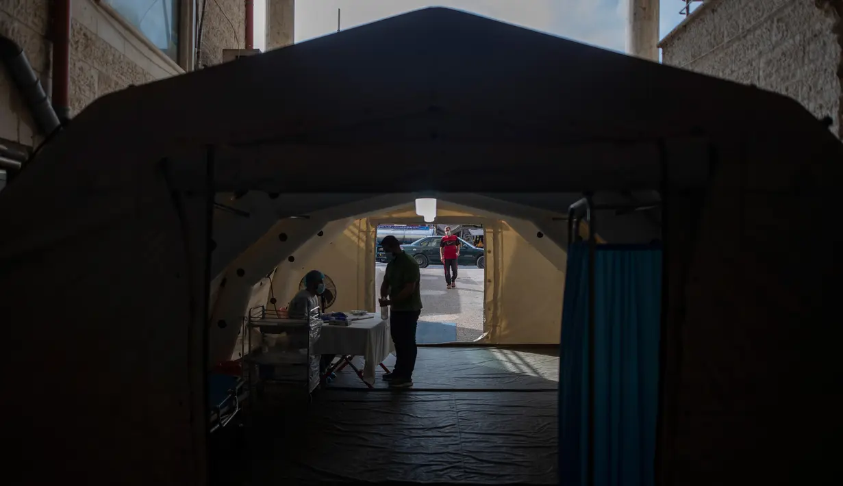 Petugas medis Palestina memeriksa suhu seseorang di dalam tenda sementara di pintu masuk Rumah Sakit al-Quds, di Kota Gaza, 7 September 2020. Lusinan petugas kesehatan garis depan telah terinfeksi COVID-19, memberikan pukulan baru ke rumah sakit yang kelebihan beban. (AP Photo/Khalil Hamra)