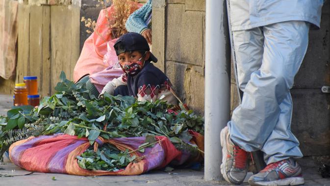 Seorang anak terlihat di mana ibunya menjual ramuan obat tradisional untuk pengobatan penyakit pernapasan di trotoar di Cochabamba, Bolivia pada 25 Juli 2020. Kasus infeksi virus corona dan kematian akibat COVID-19 semakin meningkat di negara Amerika Selatan tersebut. (AP Photo/Dico Solis)