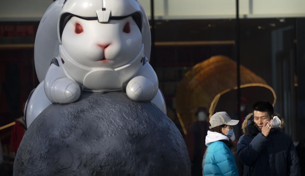 Seorang pria melepas masker saat berfoto dengan patung memperingati Tahun Kelinci di pusat perbelanjaan pada hari terakhir minggu liburan Tahun Baru Imlek di Beijing, Jumat, 27 Januari 2023. (AP/Mark Schiefelbein)